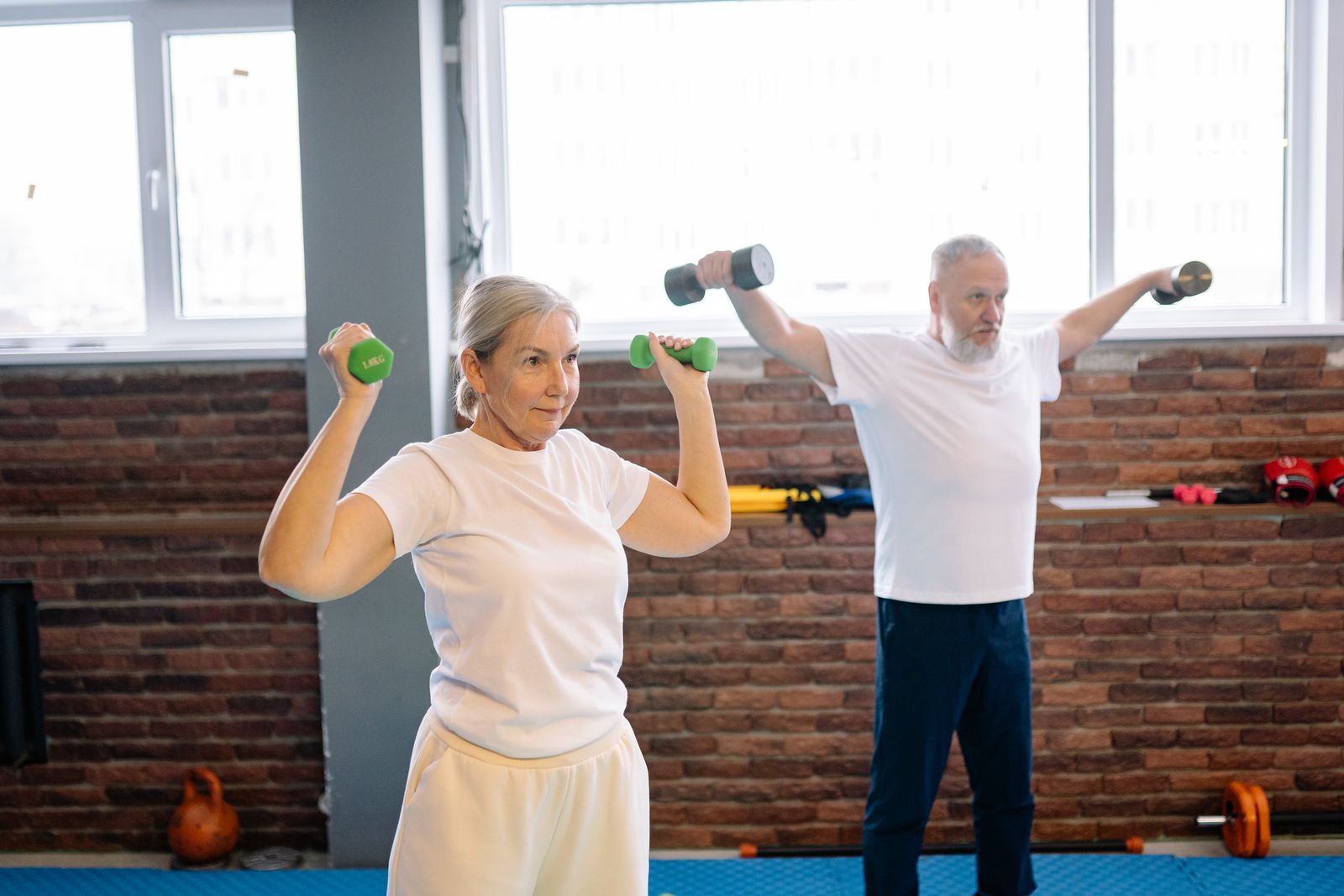 Oudere man en vrouw trainen samen met dumbbells in een lichte ruimte